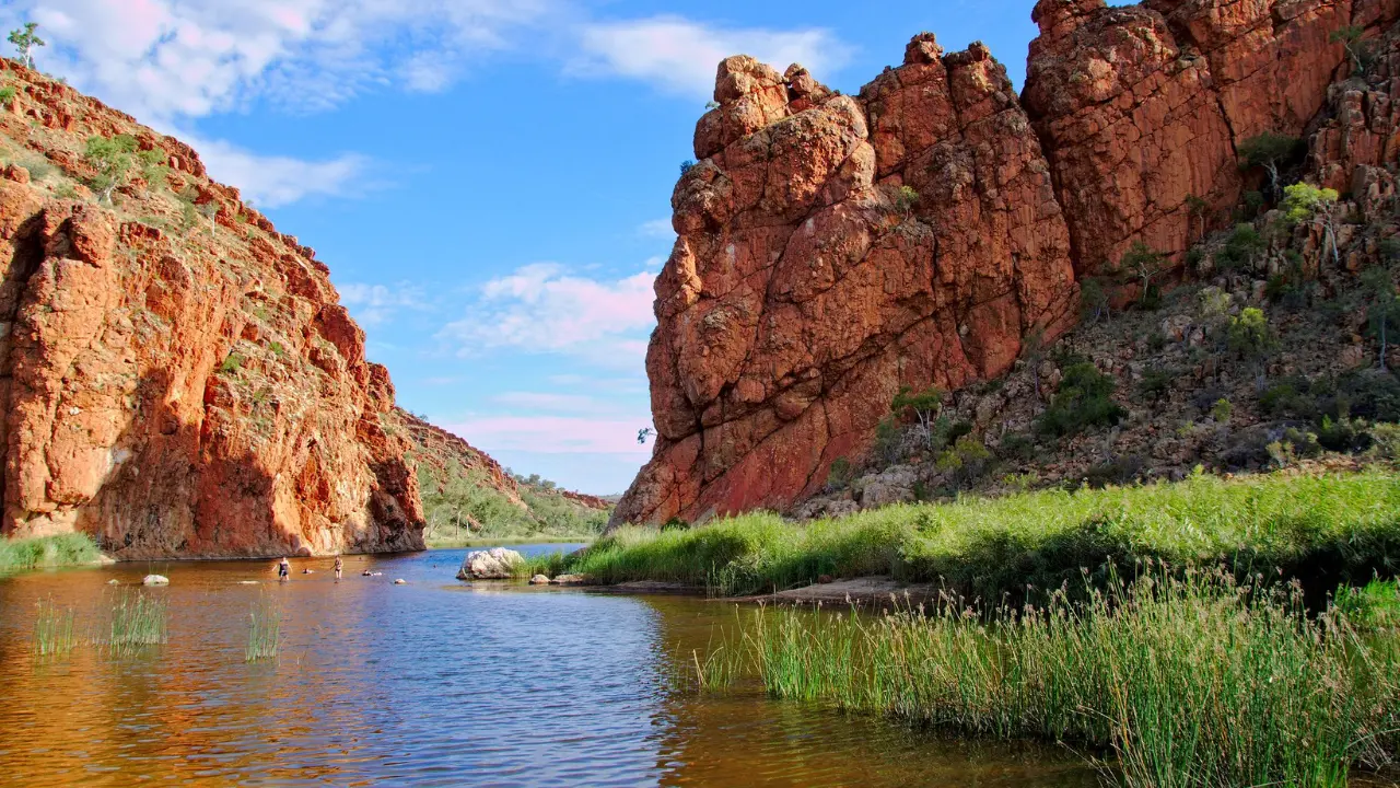 Rio Finke, na Austrália, na região do Glen Helen Gorge. Na imagem é possível ver paredões de pedra dos dois lados do rio. Nas margens do rio Finke, na base dos paredões de pedra, é possível ver uma vegetação verde.