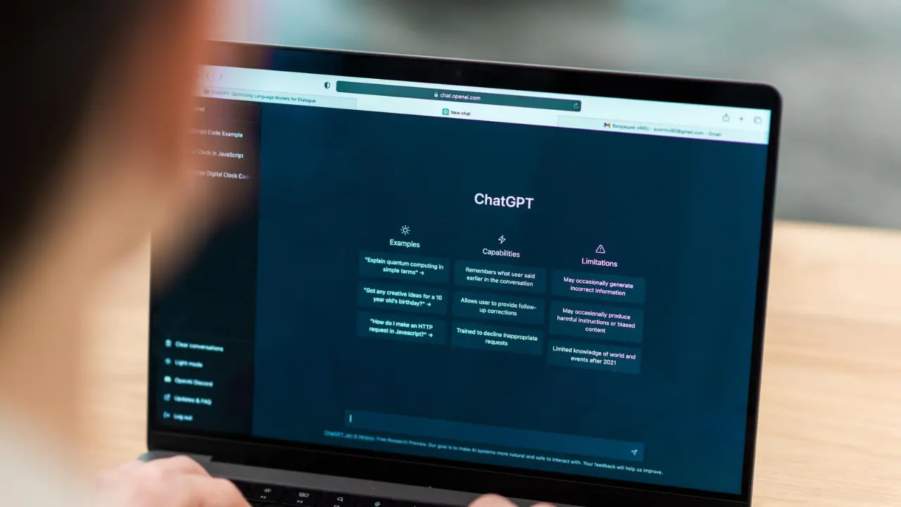 Pessoa utilizando um laptop que exibe a interface do ChatGPT na tela. A interface apresenta seções sobre exemplos, capacidades e limitações da IA.