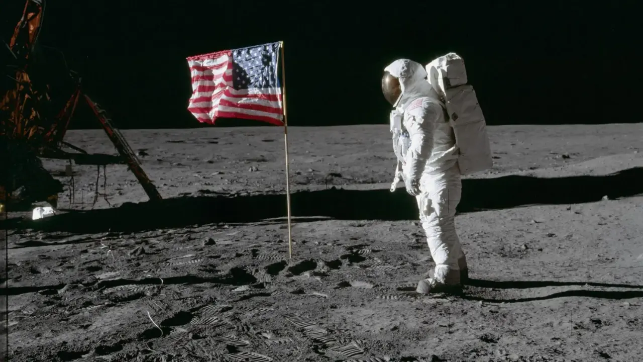 Astronauta Buzz Aldrin na lua, ao lado da bandeira dos Estados Unidos, fincada no sol lunar.