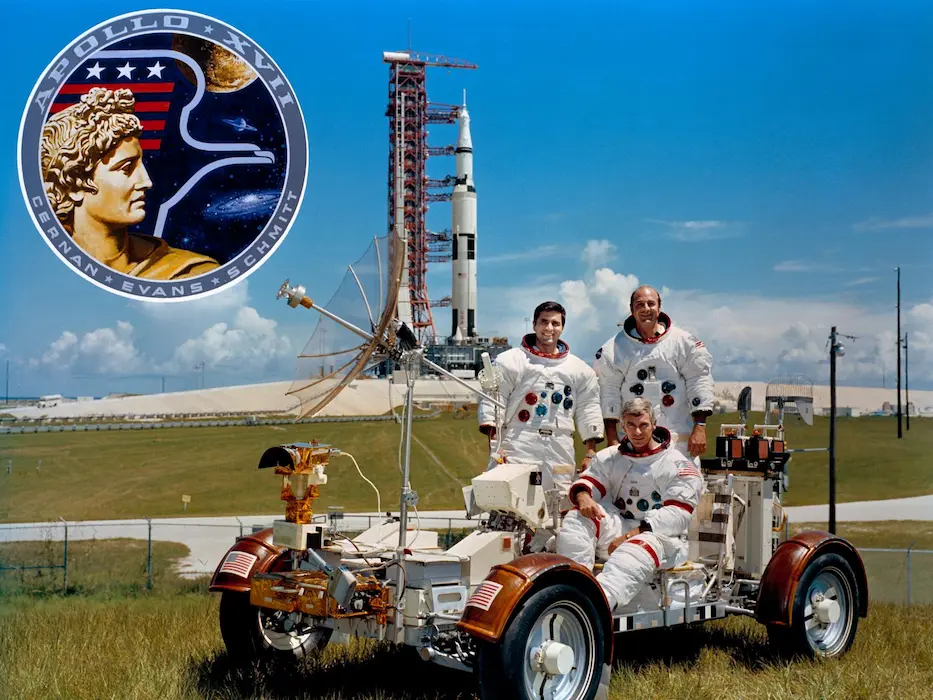 Tripulação da Apollo 16 em treinamento em um veículo lunar. Estão na imagem Eugene A. Cernan (sentado), Ronald E. Evans (em pé à direita) e Harrison H. Schmitt (em pé à esquerda).